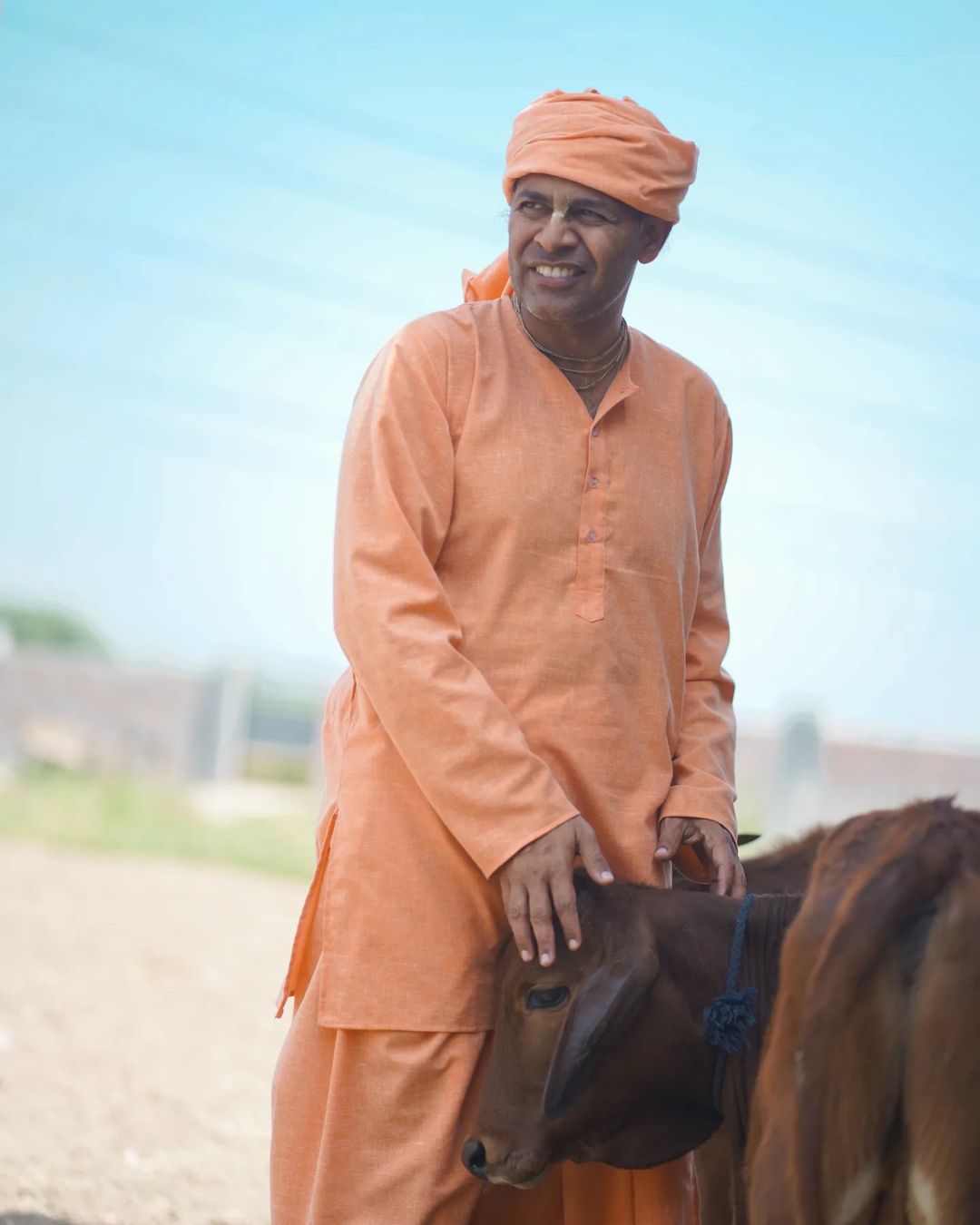Dr. Keshav Anand Das smiling with a calf at the farm community